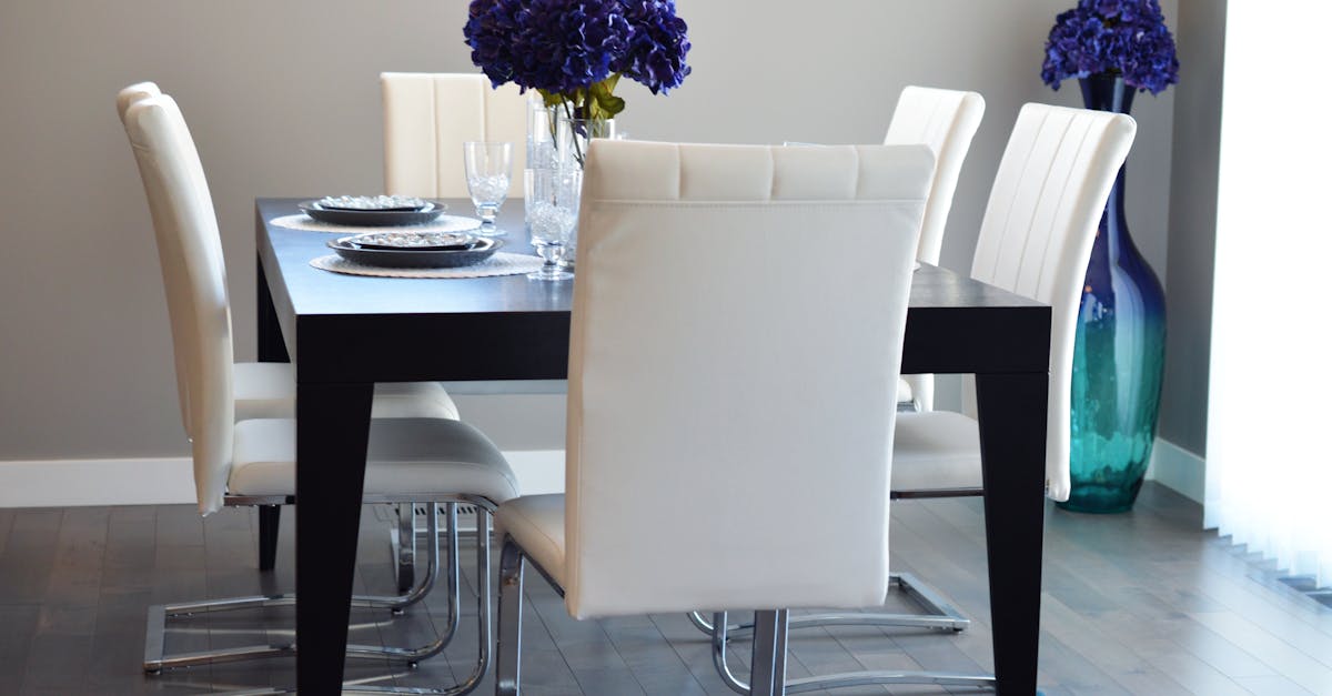 A stylish, contemporary dining room featuring elegant white chairs and a dark wooden table adorned with purple flowers.